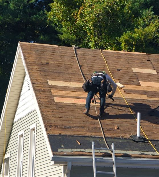 Roof replacement in progress in Mystic, CT with contractor removing old shingles and preparing the roof deck.