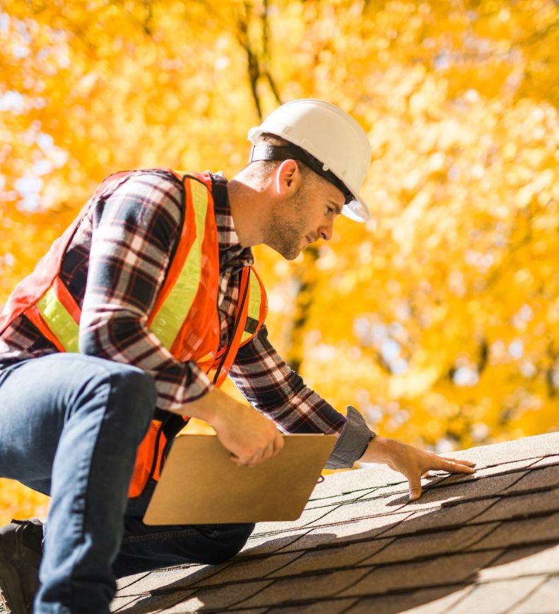 Roof inspector checking asphalt shingles with a clipboard during a home inspection in fall.